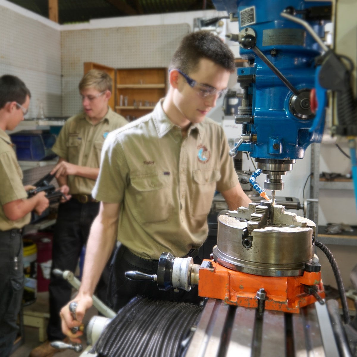 Three individuals in a workshop setting with machinery and tools.