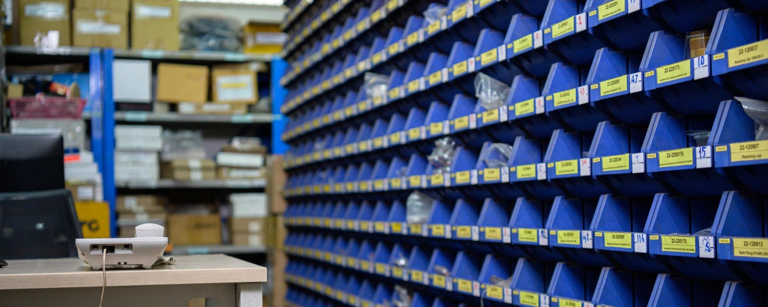Warehouse storage area with shelves stocked with blue bins and labeled boxes.