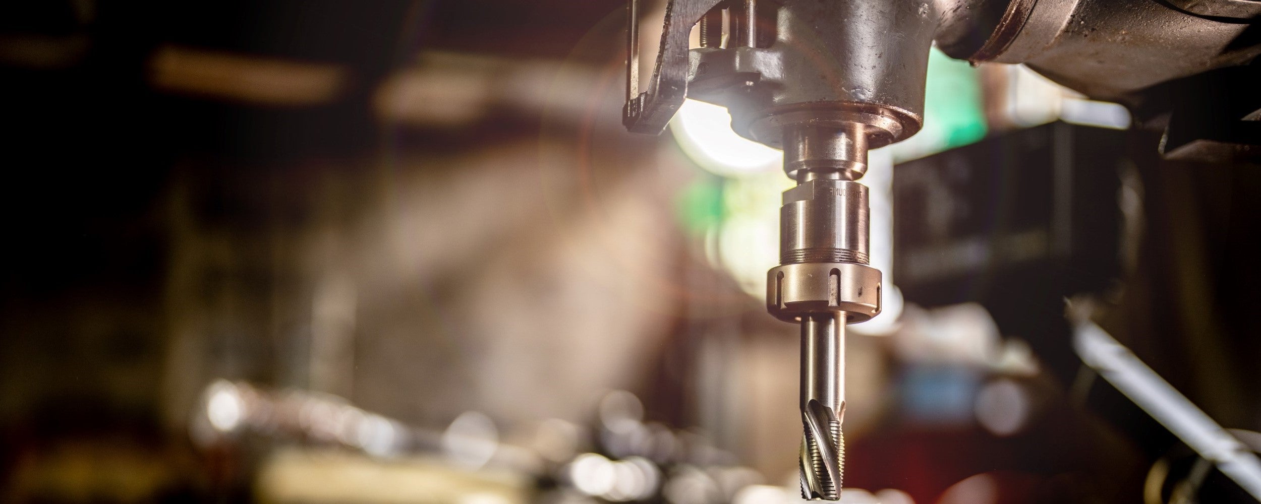 Drill bit being used on a drill machine with a blurred workshop background